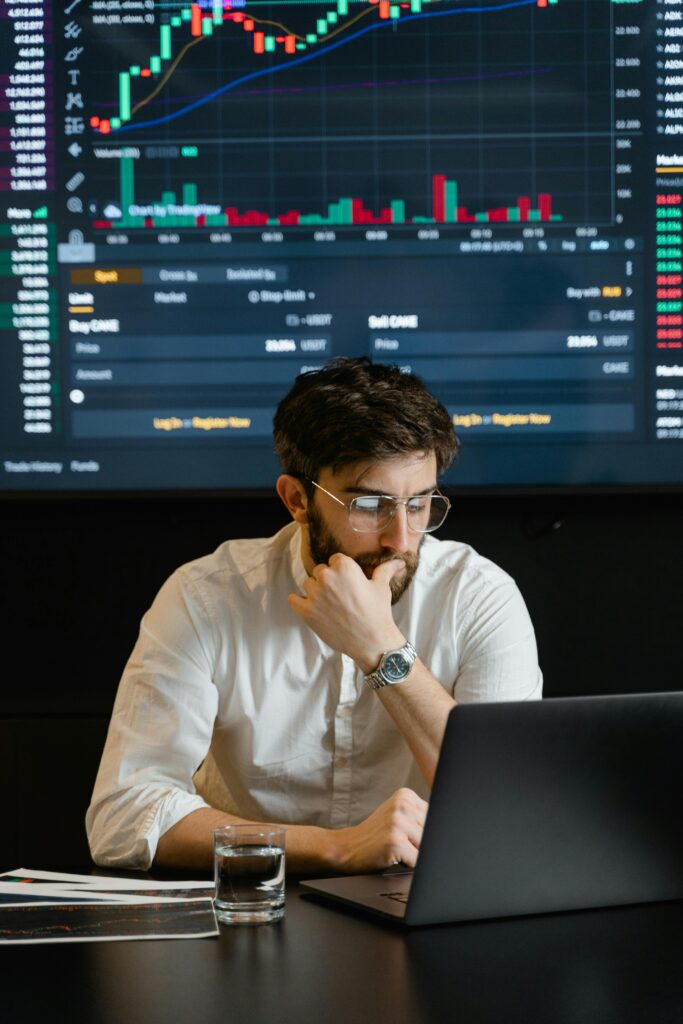 Pensive businessman with a beard analyzing stock market trends on a laptop in an office setting.